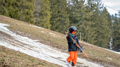 Child with skis walking down a grassy hill